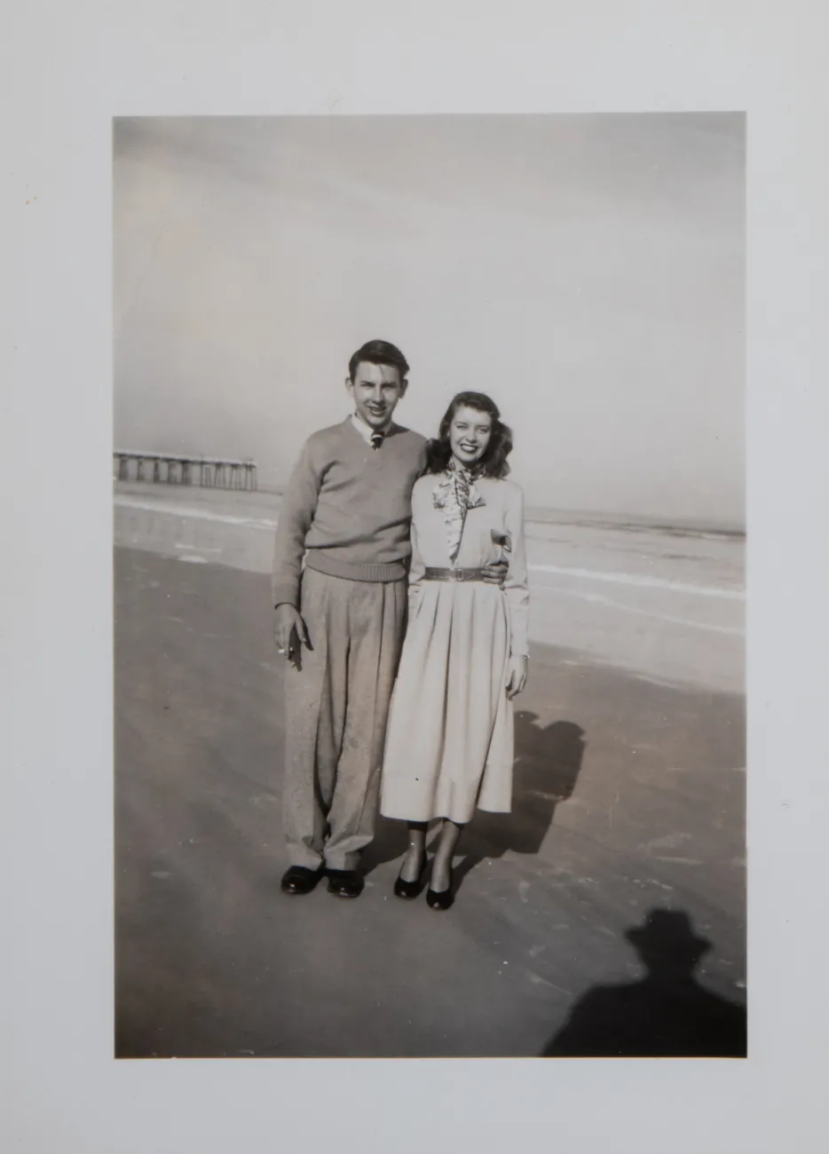 A black and white photograph of Jim and Alice Clark in their early twenties. They smile happily on the beach during their honeymoon.